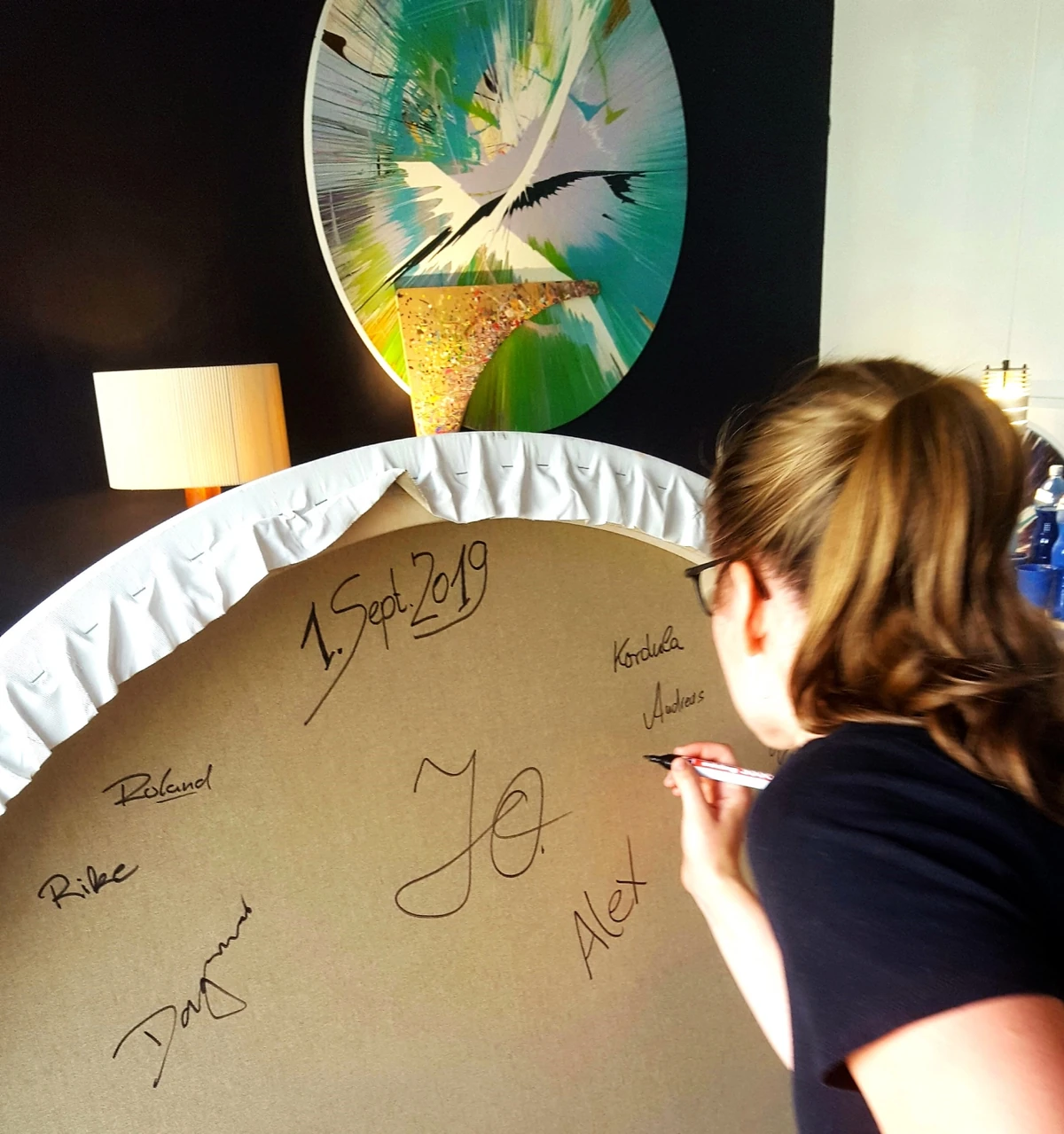 Teilnehmerin signiert das gemeinsam gestaltete Spin Painting eines Teamevents