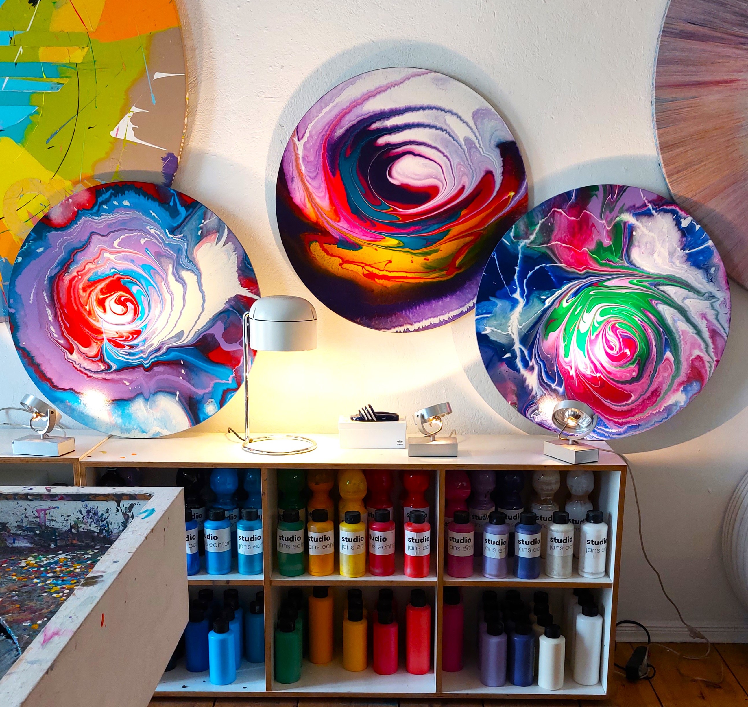 Drei runde farbenfrohe Spin Paintings über dem Farbregal im Studio