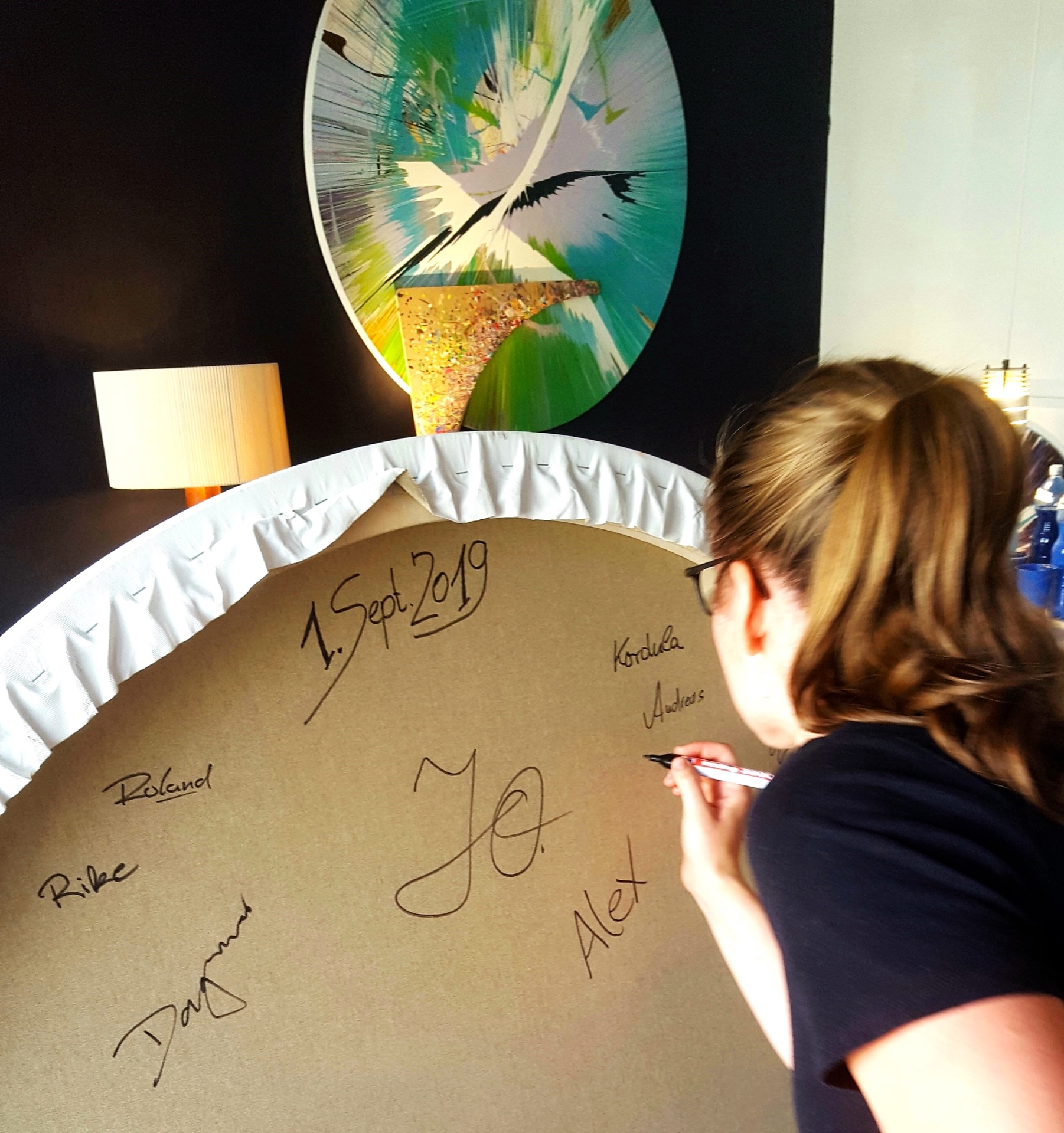 Teilnehmerin signiert das gemeinsam gestaltete Spin Painting eines Teamevents