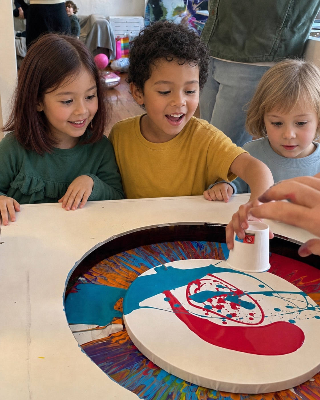 Drei Kinder beobachten begeistert ein farbiges Spin Painting