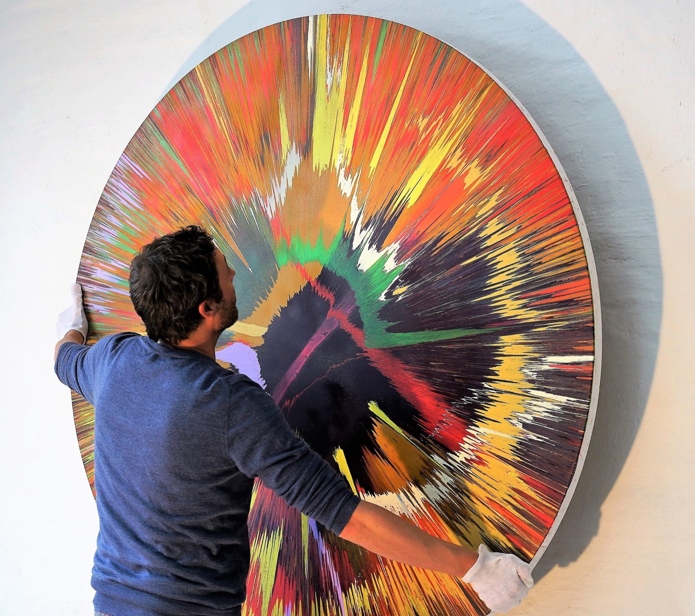 Jans Echternacht wearing white gloves in front of a large-format spin painting